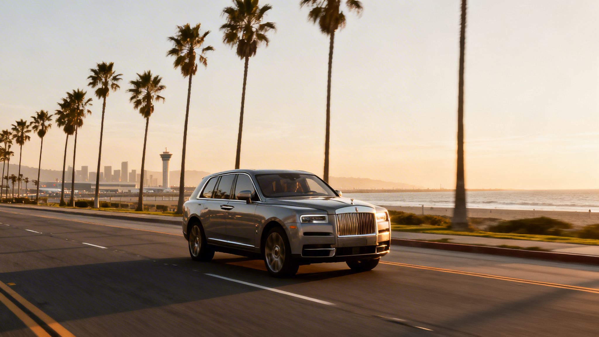 Silver Rolls-Royce Cullinan drives on a coastal road at sunset, with palm trees, city skyline, and ocean.