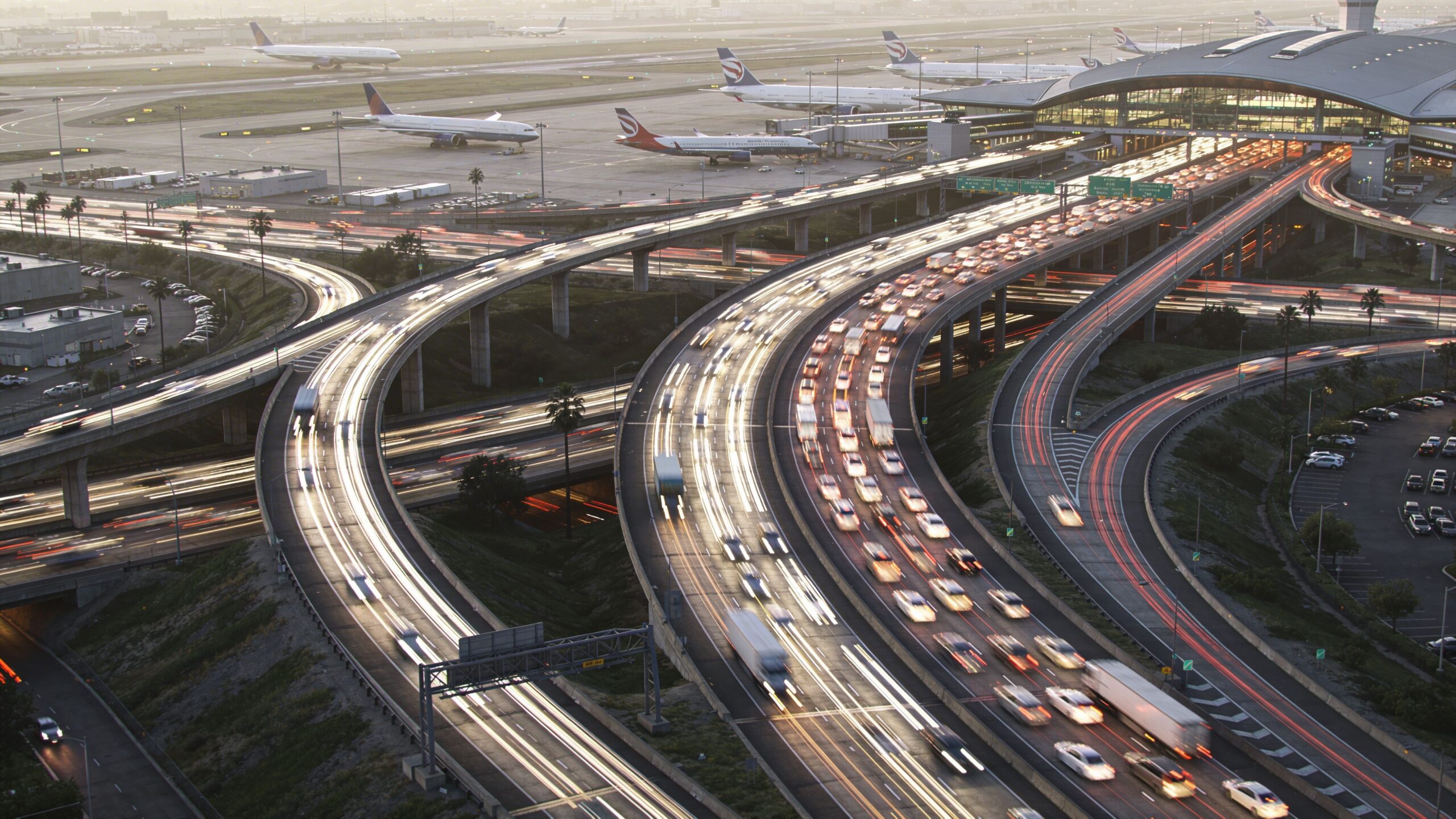 A high-angle view of a bustling airport highway at dusk with light trails from moving traffic.