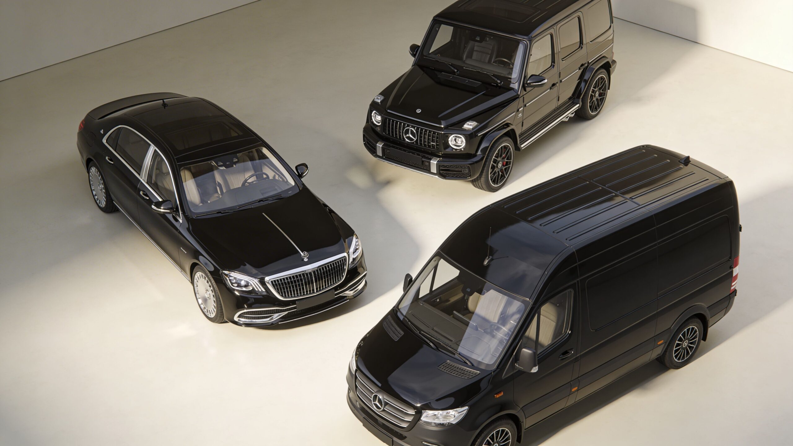 A high-angle view of three luxury black Mercedes-Benz vehicles parked on a clean, light concrete floor.